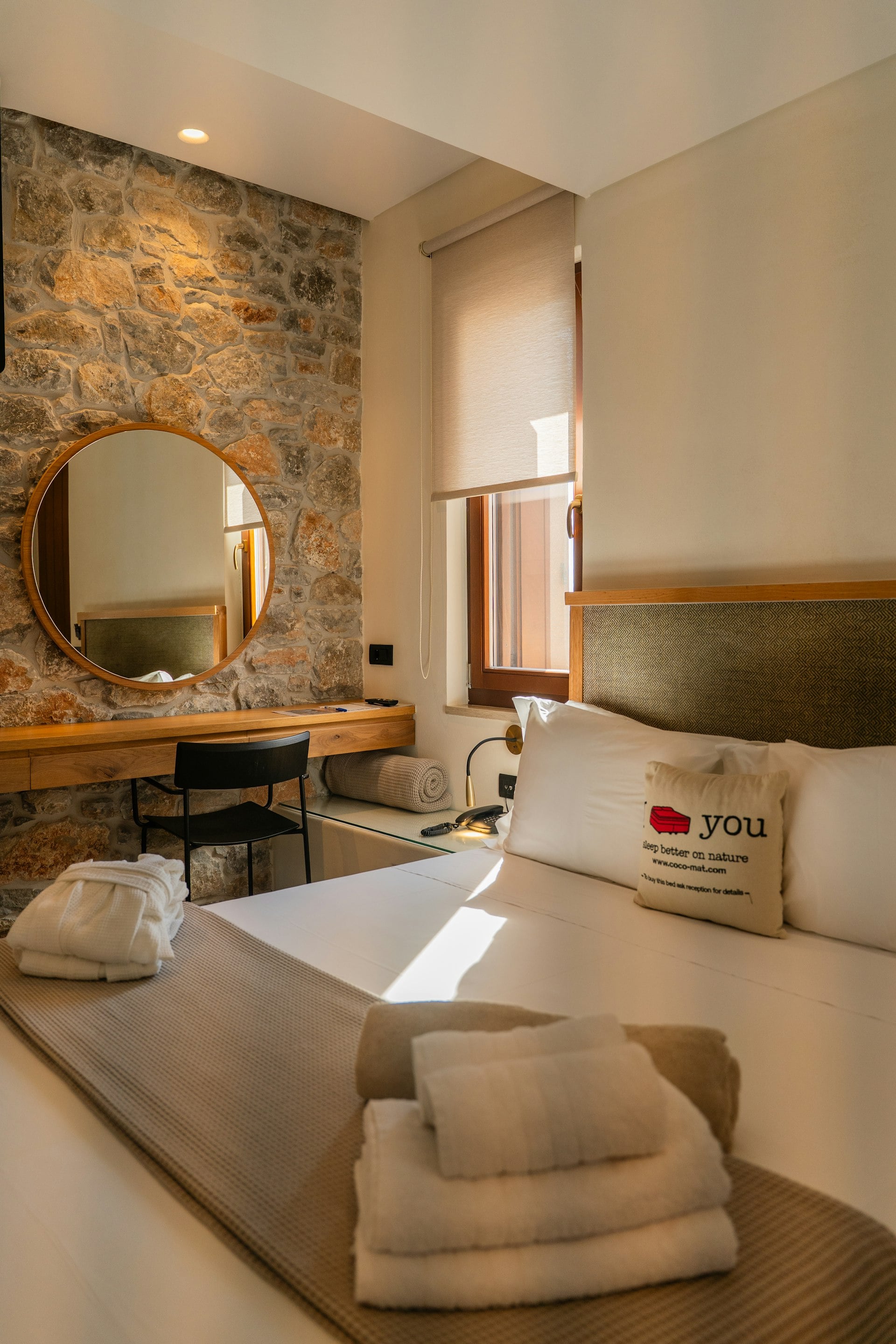 A calm bedroom with a stone wall and a round mirror
