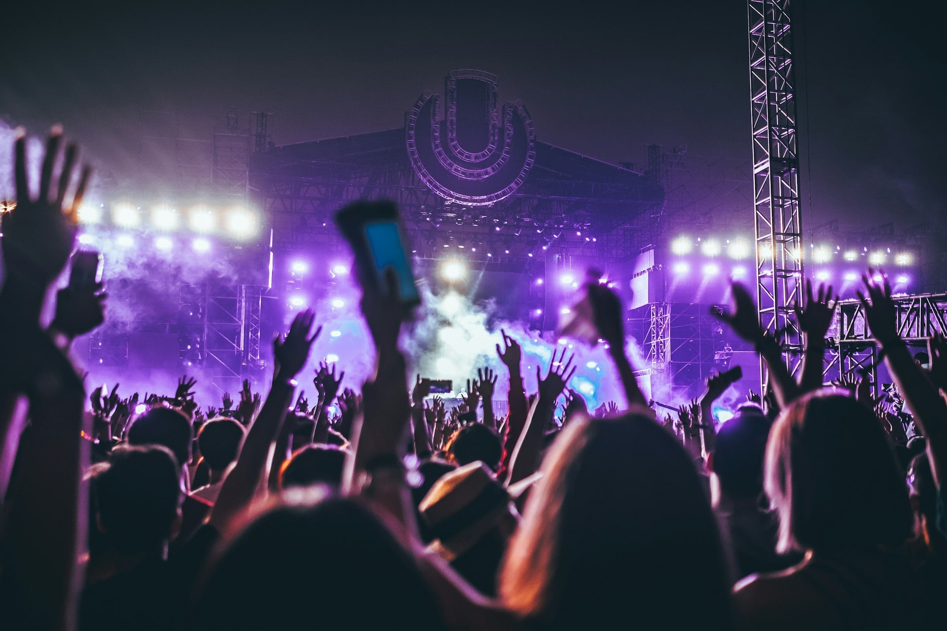 A crowd with hands raised under purple stage lights